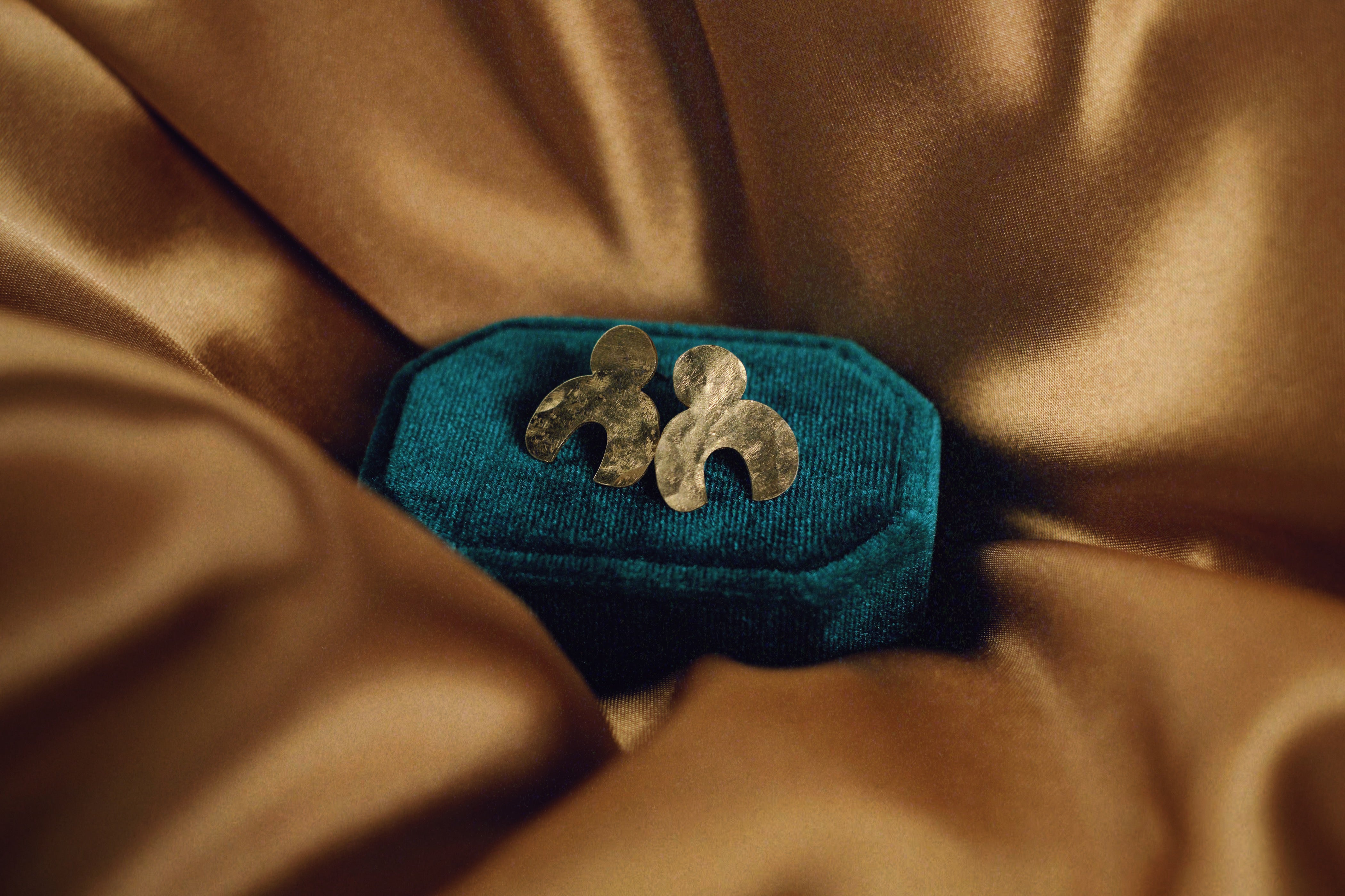 Hand hammered vermeil post earrings handmade by Tasha Bundy in Tucson, sitting on a teal cushion in a gold silk sheet