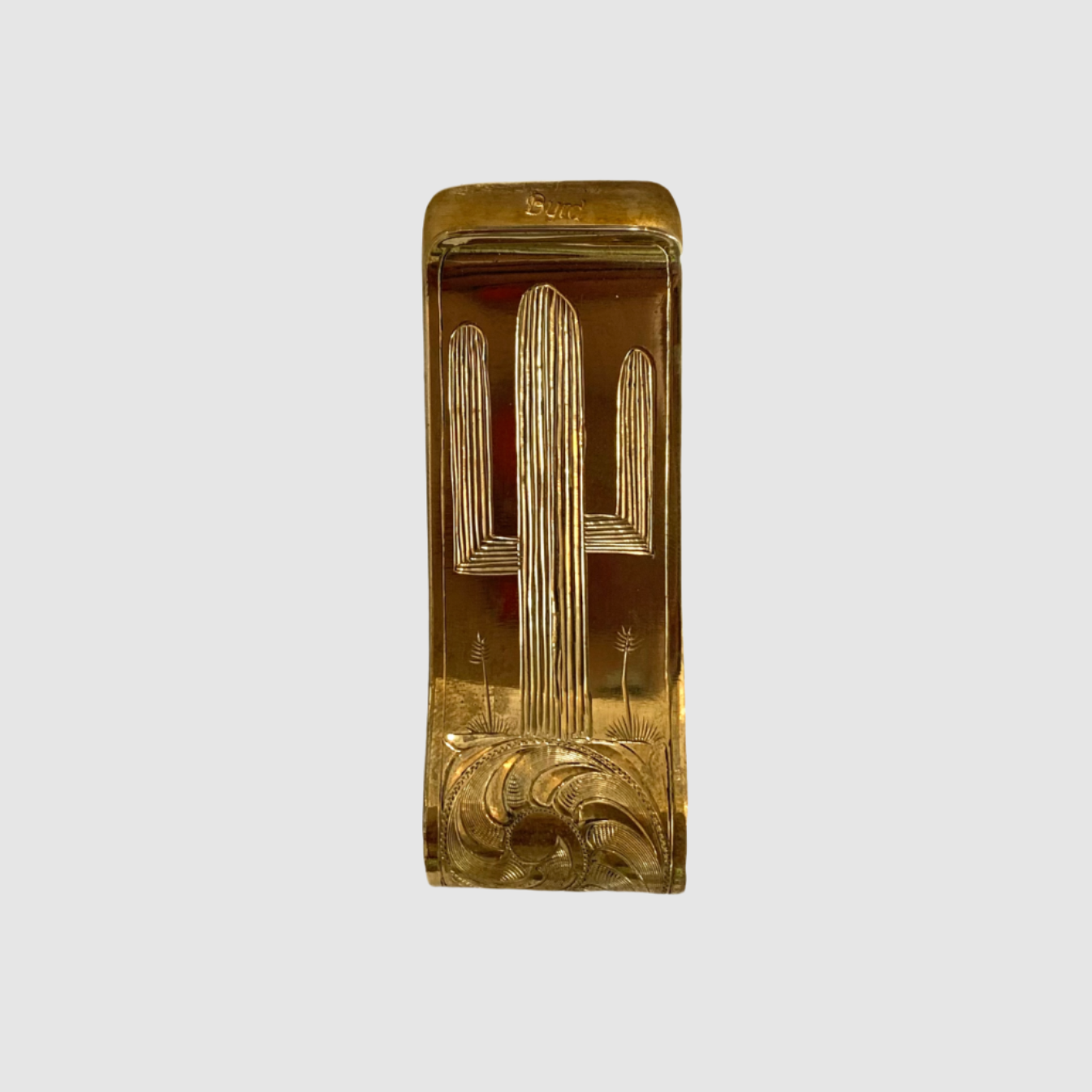 A brass money clip with a hand-engraved Saguaro design on a white background.
