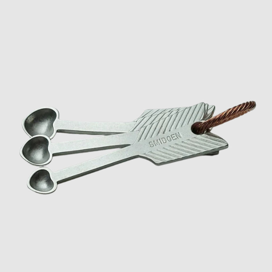 Set of metal measuring spoons with a brand name on a light surface.
