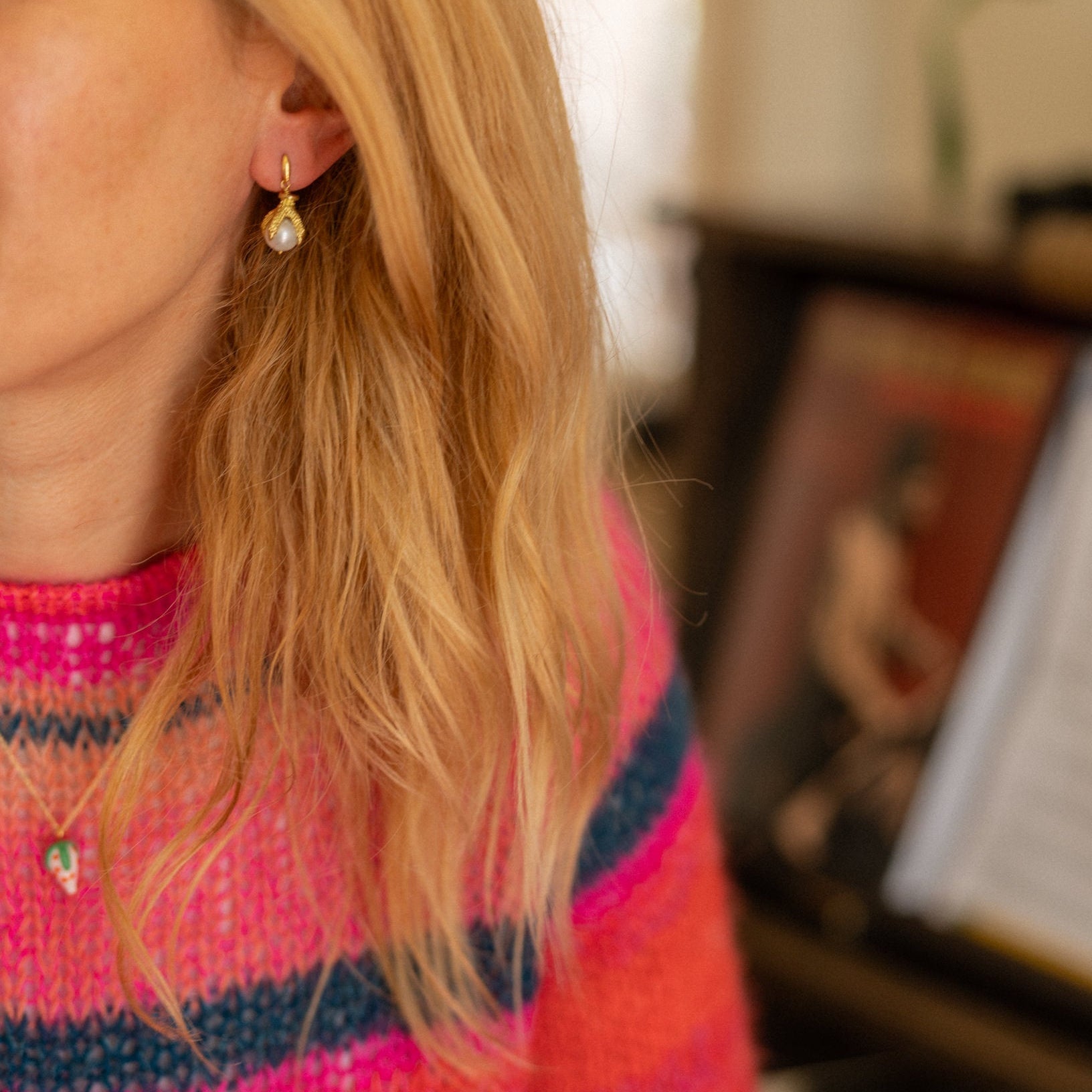 Woman wearing a colorful striped sweater in an indoor setting with a blurred background wearing Tasha Bundy's handmade jewelry. Pearl and glass, vermeil and brass components.