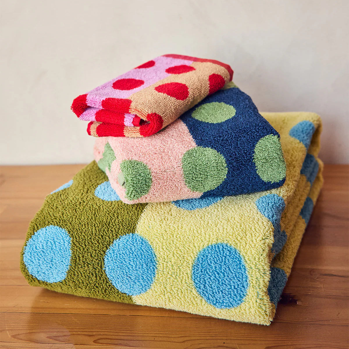 Stack of colorful polka dot towels on a wooden surface with a neutral background