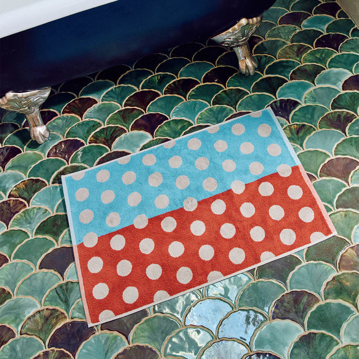 Polka dot rug on a tiled bathroom floor with a bathtub.