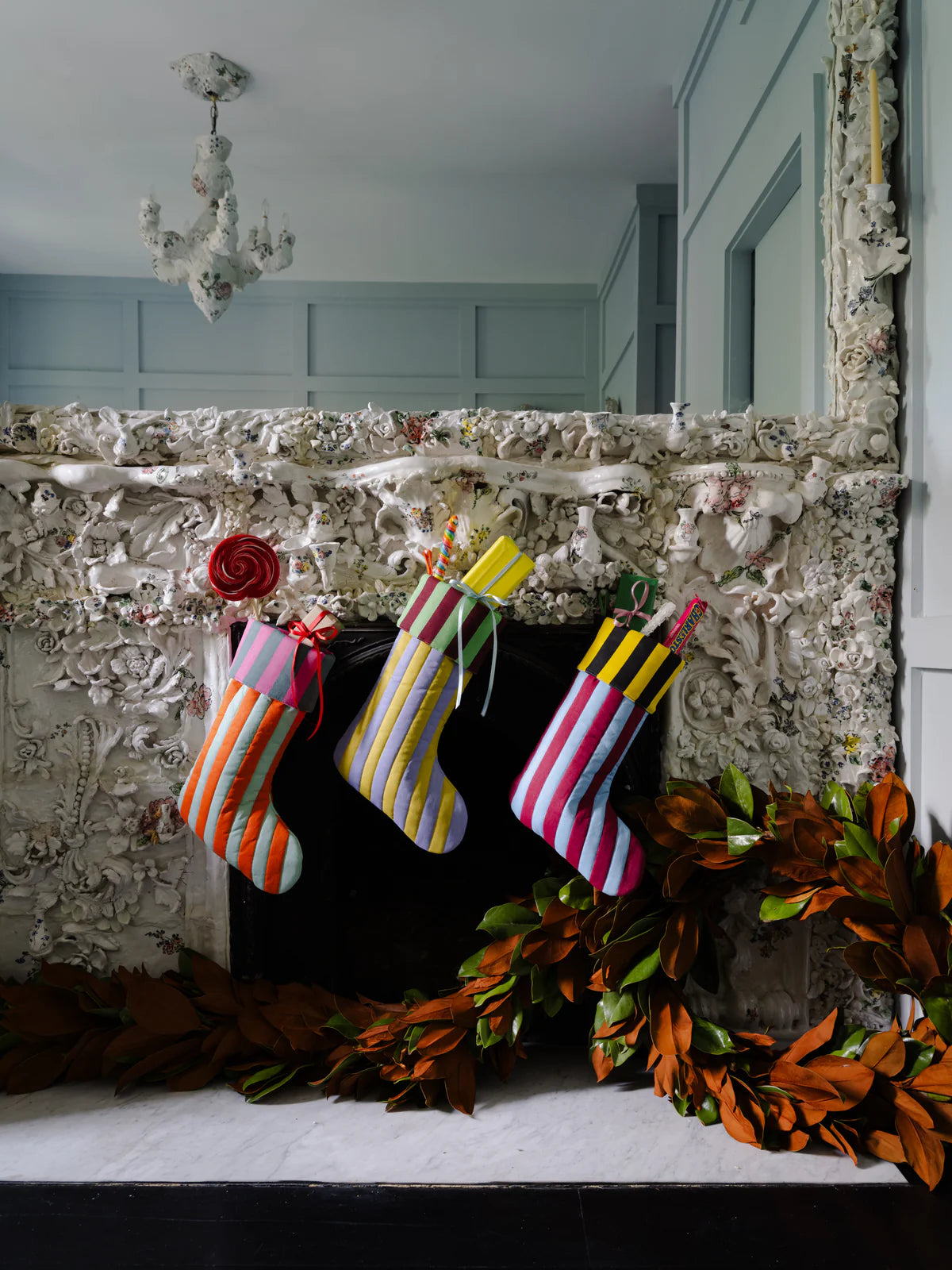 3 quilted cotton holiday stockings stuffed with presents hung by a fabric loop on a mantle. Striped, multi colored pattern on each.