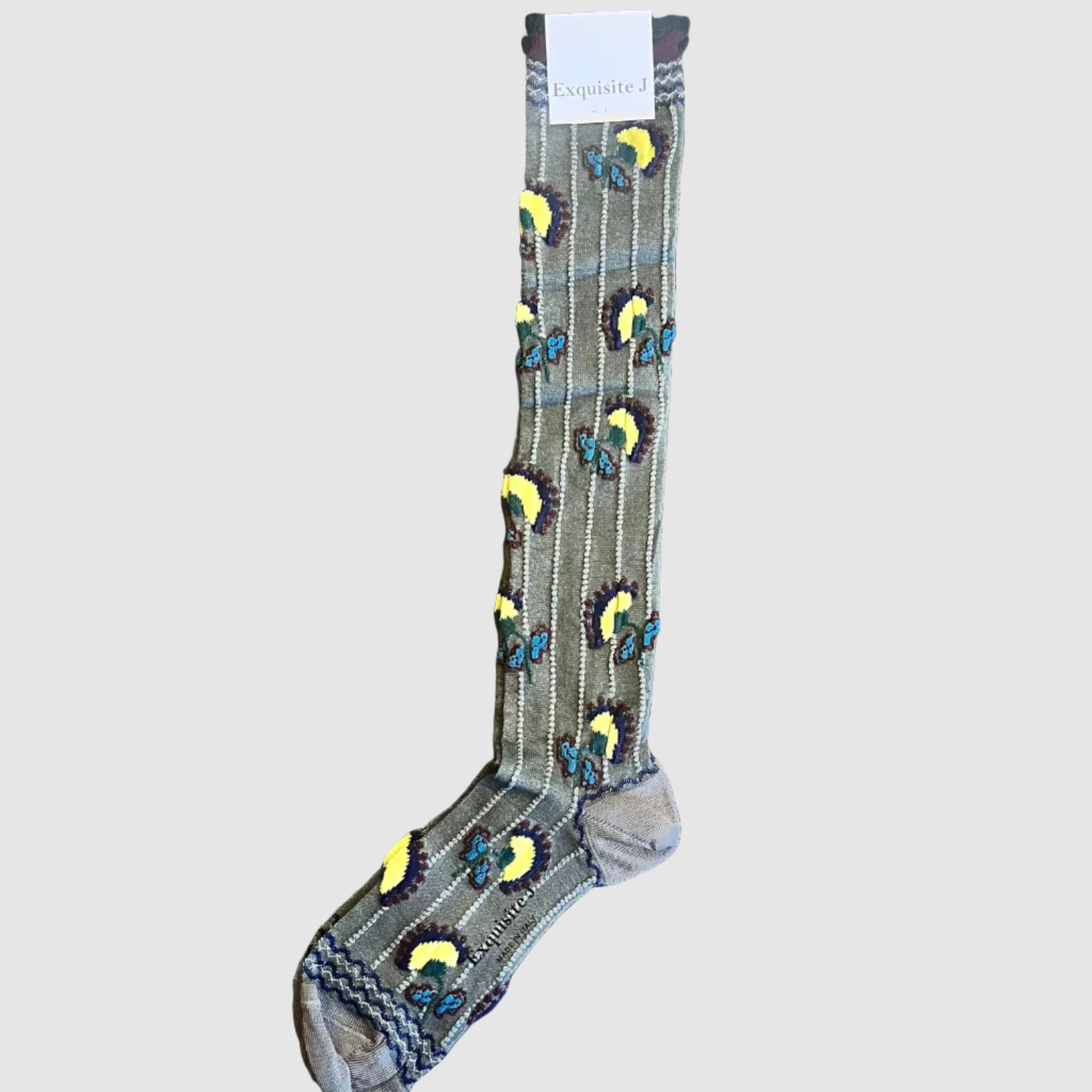 A single patterned sock laid flat on a dark rustic wooden surface. The sock has a gray base with vertical white stripes and repeated embroidered motifs in yellow, blue, and dark brown, plus a gray and white braided cuff.