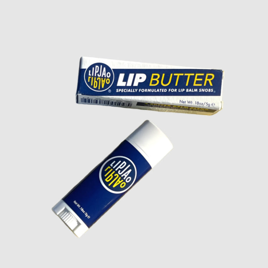 One .18oz tube of the LipJao lip balm and it's cardboard box packaging that reads "Lip Butter, specially formulated for lip balm snobs." in yellow, white and blue. Both are floating on a grey background.