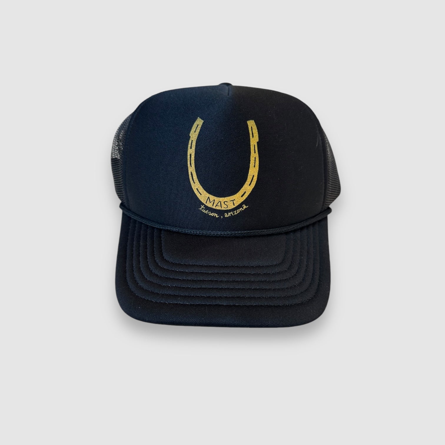 Black baseball cap/trucker hat with foam front and mesh back.  Hand drawn yellow horseshoe design, facing up with MAST in center and Tucson, Arizona  printed below. 