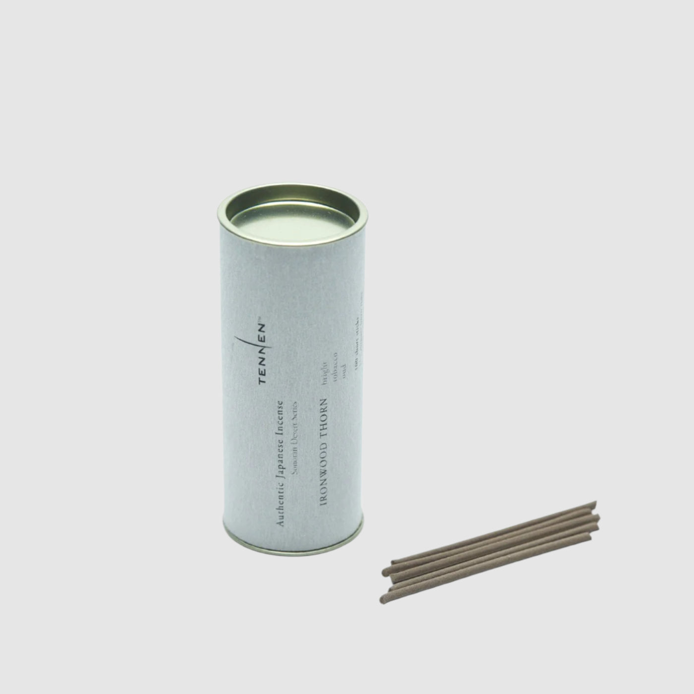 Canister of Tennen Ironwood Thorn Incense next to a few loose sticks of incense on a grey background. 