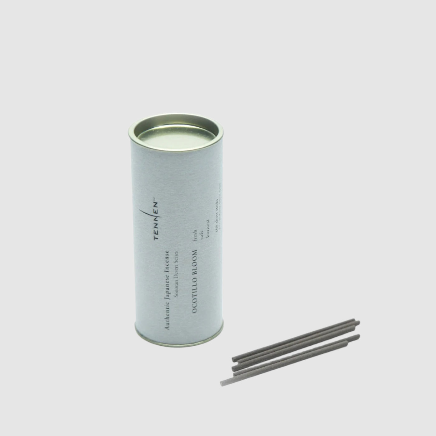 Canister of Tennen Ocotillo Bloom Incense next to a few loose sticks of incense on a grey background. 