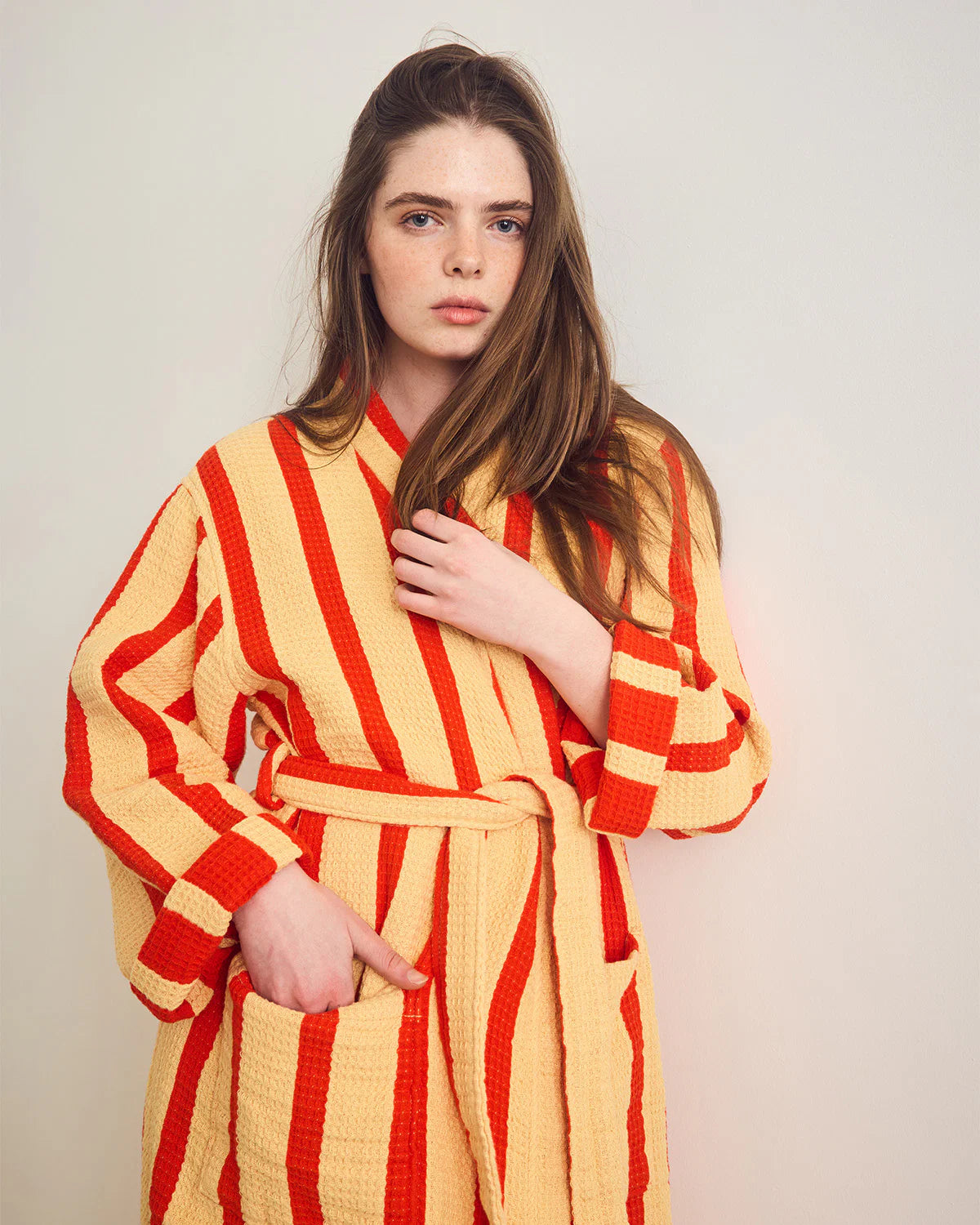 Woman wearing a yellow and red striped robe against a plain background
