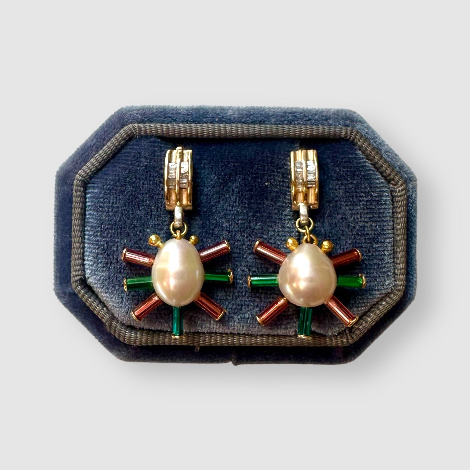 Pair of earrings handmade by Sofie Albertsen in Tucson, Arizona. Pearl center with vintage glass beads strung on a vintage diamond bracelet piece. Displayed on a blue cushion on a light grey background.