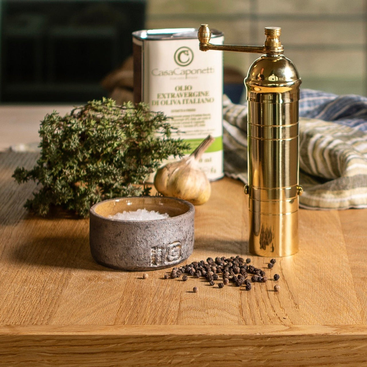 Gold pepper grinder with a bowl of salt and peppercorns on a wooden surface.