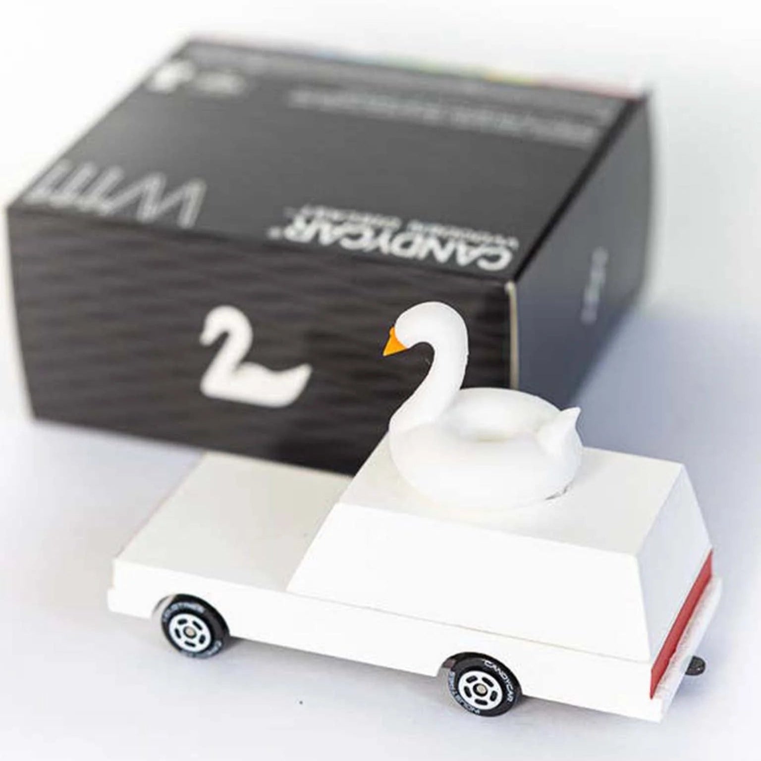 White swan-shaped candle with red stripe on a white surface, next to a black box