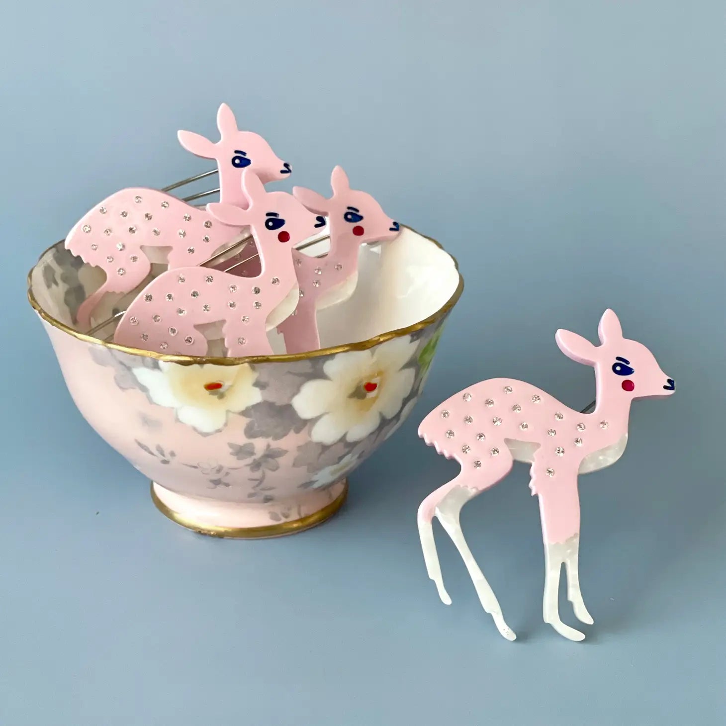 Pink, Centinelle deer barrettes on a light blue background. Three are in a teacup, one is outside the cup. 
