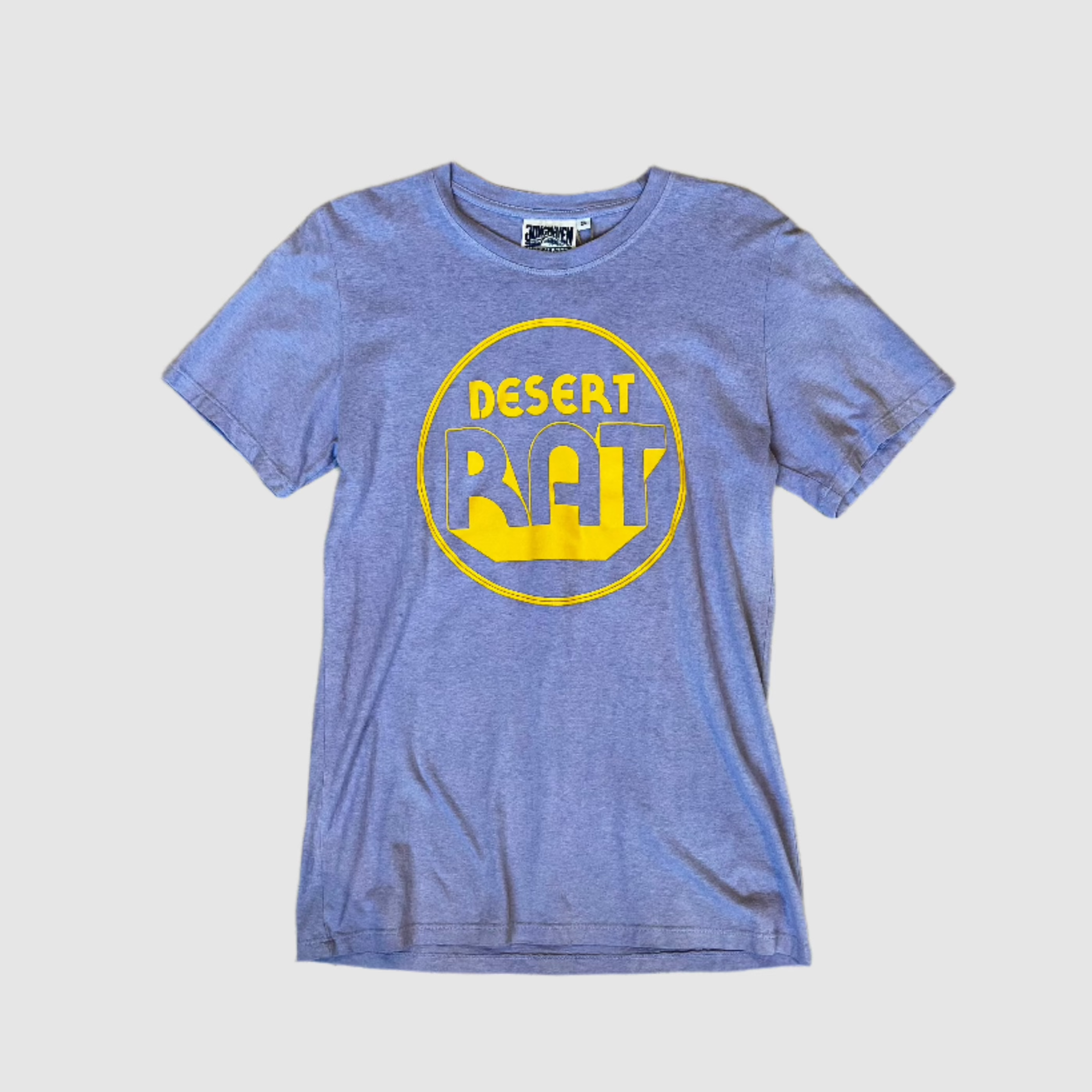 Front of a lavender colored t-shirt with "desert rat" circular, yellow colored logo centered on shirt. Gray background