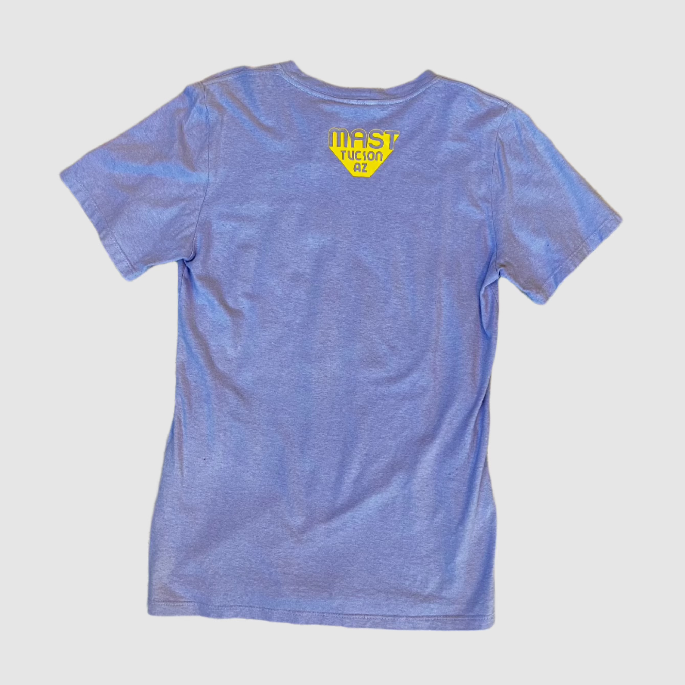 Back of lavender colored t-shirt with "MAST Tucson AZ" yellow colored logo centered towards top of shirt. Gray background