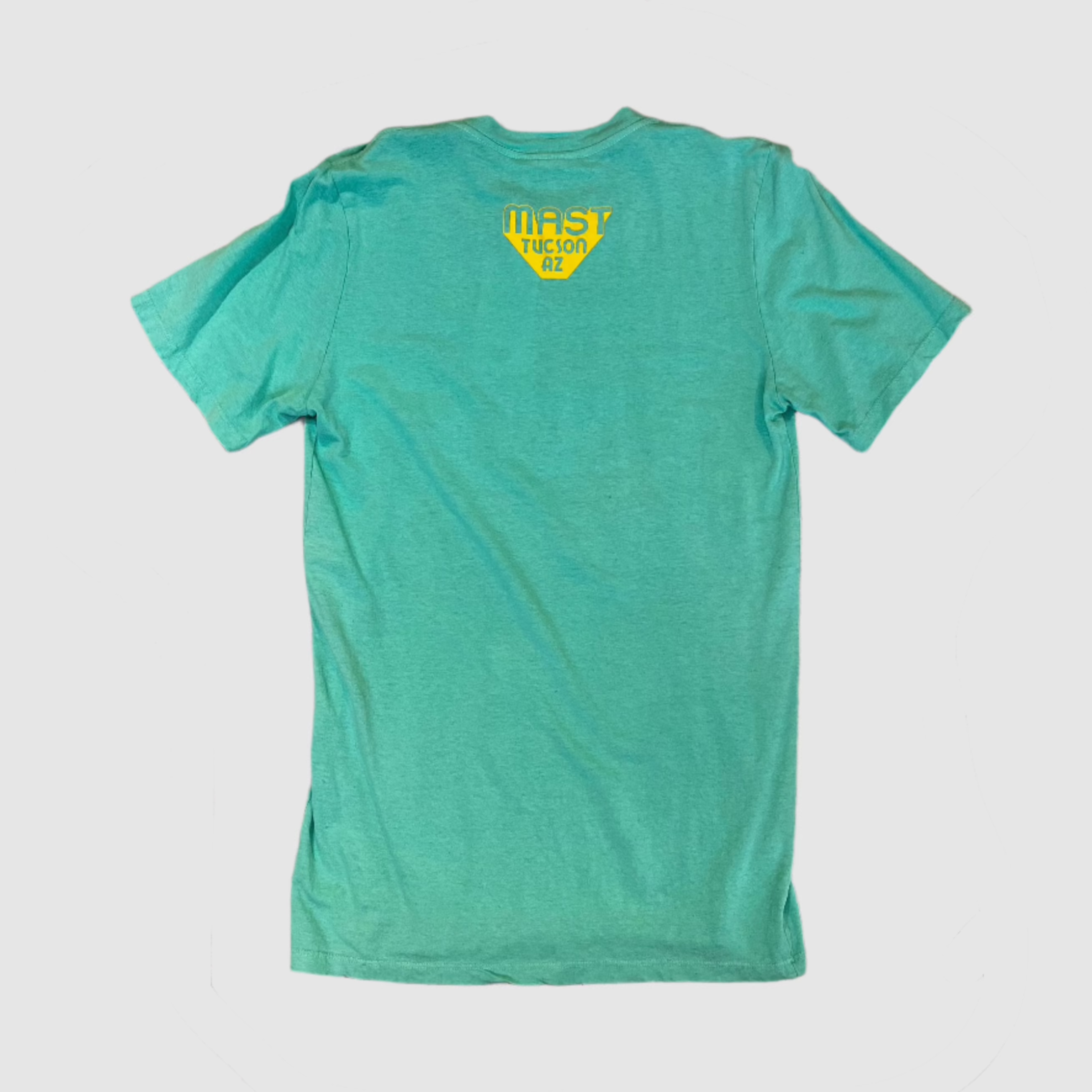 Back of seafoam green colored t-shirt with "MAST Tucson AZ" yellow colored logo centered towards top of shirt. Gray background