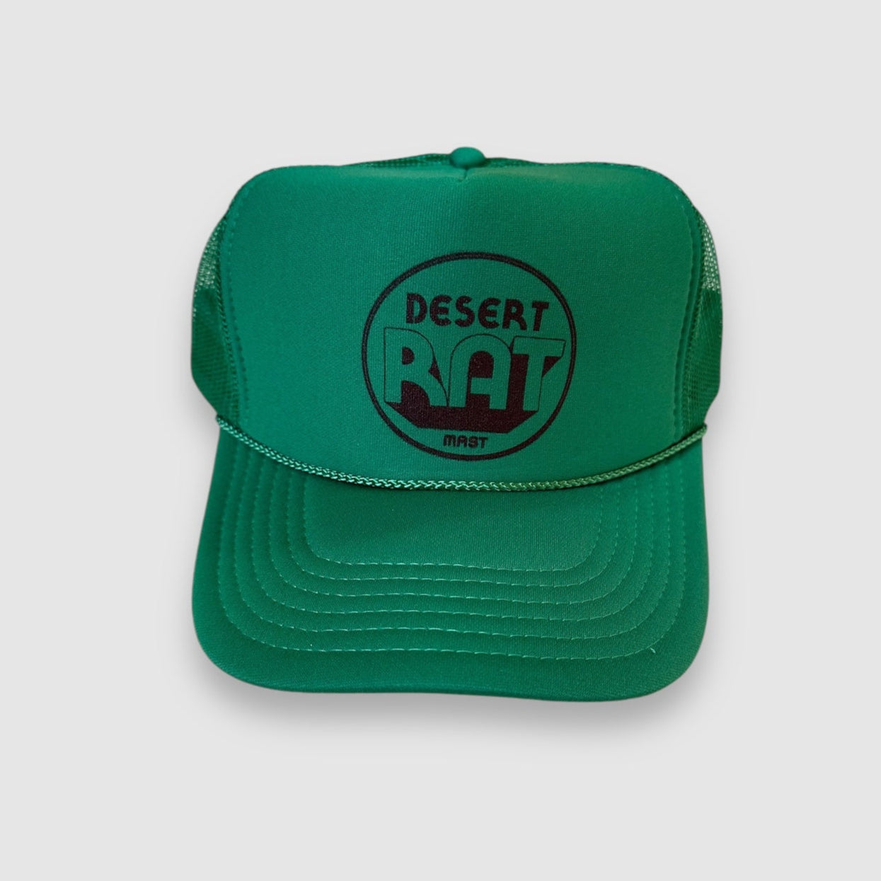 Front view of a classic green truckers cap with polyester foam front and mesh back. "Desert rat" in circular brown print on front of hat with "MAST" printed smaller underneath. 