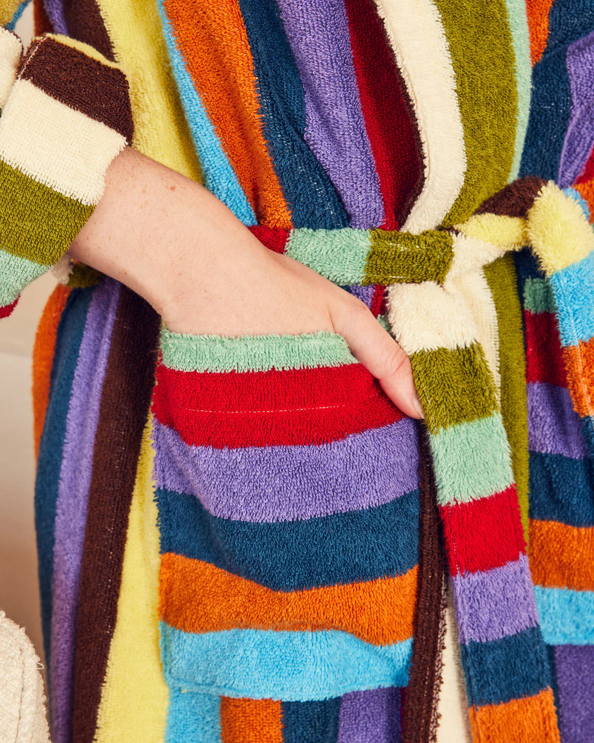 Close-up of a hand in the pocket of the Dusen Dusen multicolored striped robe with a belt