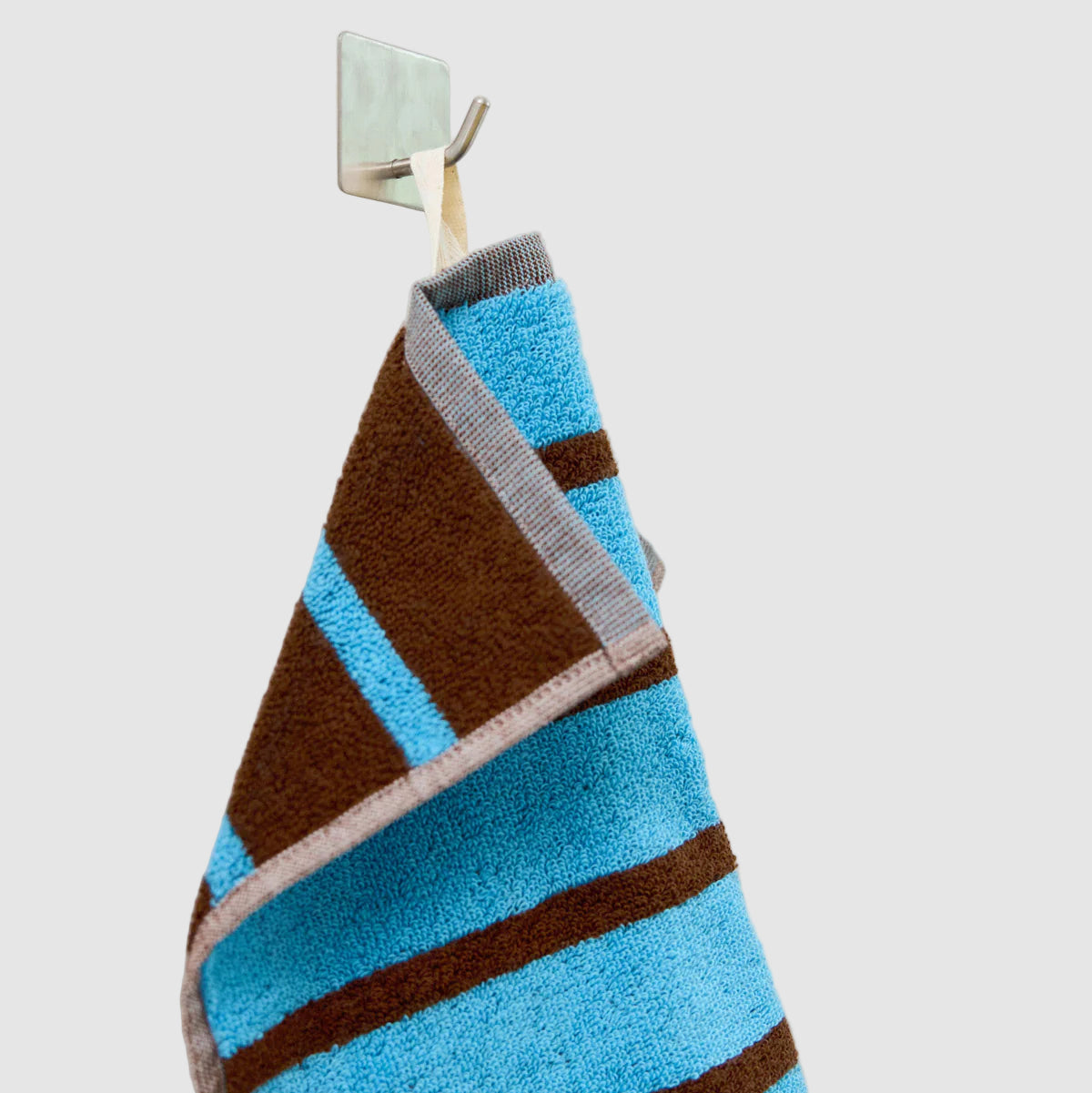 Striped blue and brown Dusen Dusen wash cloth hanging on a hook against light grey "wall" background