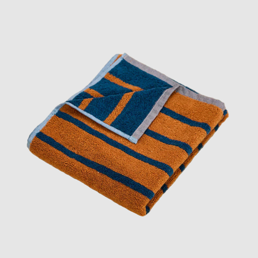 Folded dusen dusen hand towel with blue and orange stripes on a light gray background