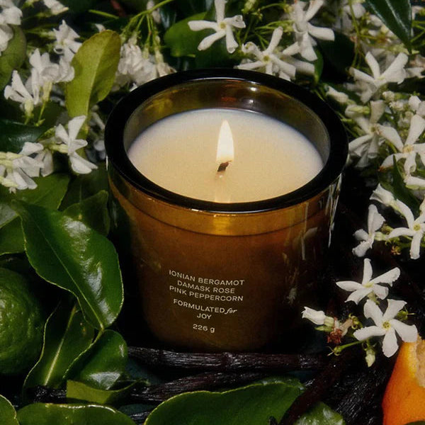 Flamingo Estate "Coriandoli" scented candle in "field" with flowers and leaves in the background