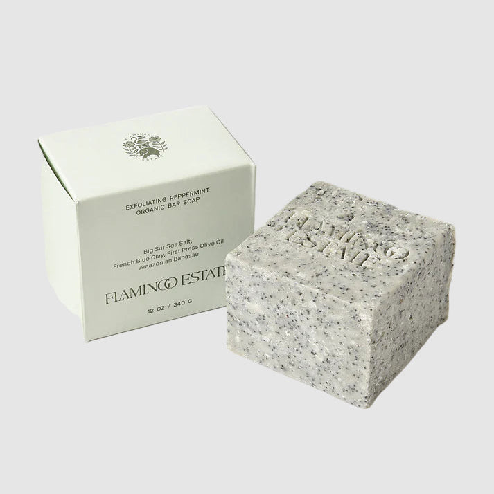 An exfoliating peppermint soap brick with the brand name "Flamingo Estate" stamped into the soap and it's packaging on a light grey background