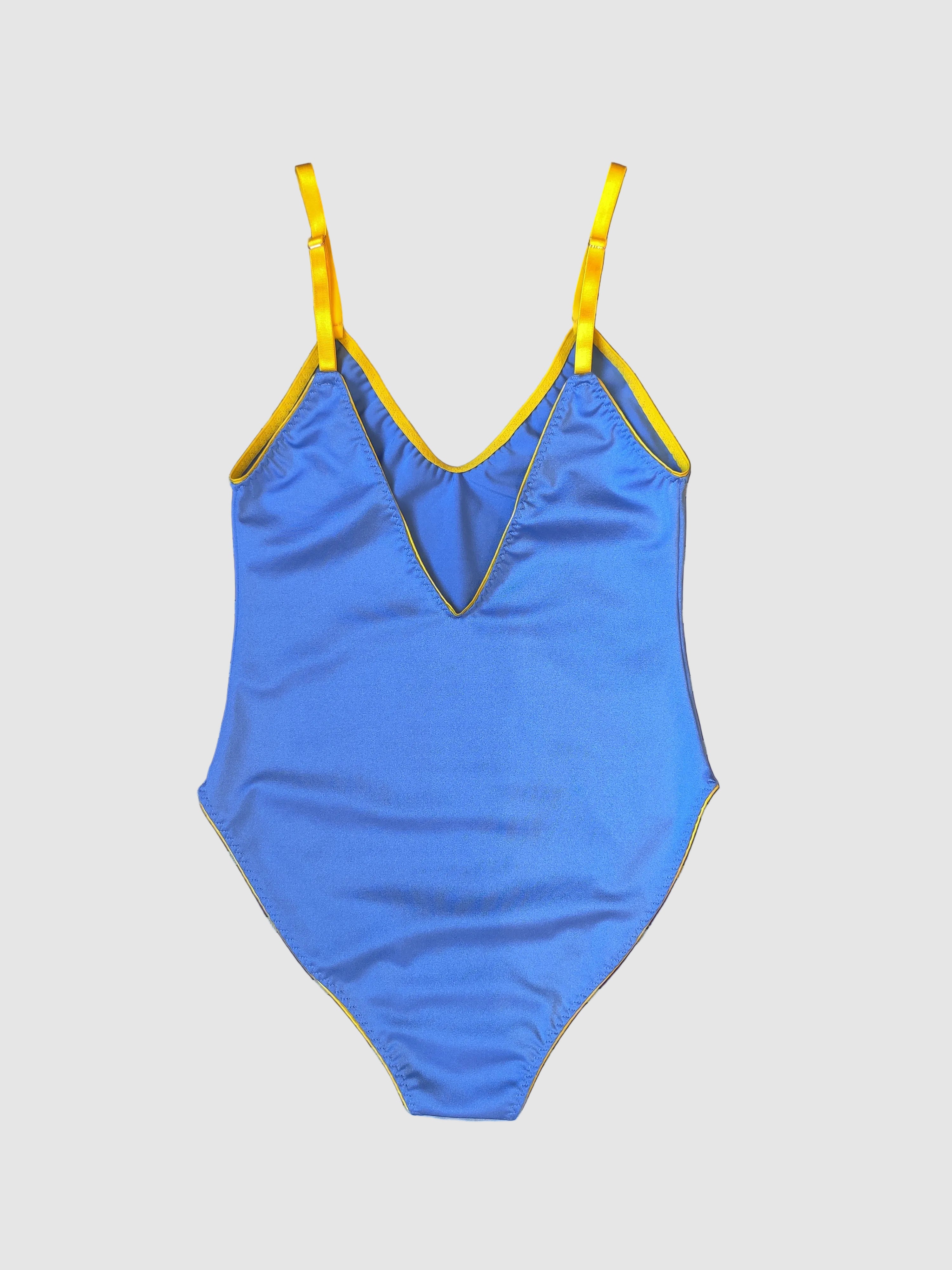 A blue one-piece swimsuit with yellow trim and straps, laid flat on a dark purple and white striped fabric background.