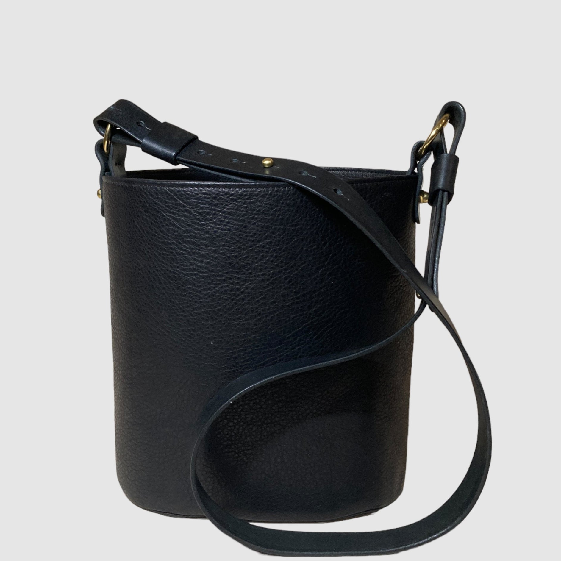 Matte black leather bucket bag with an adjustable leather strap and brass acorn detail.