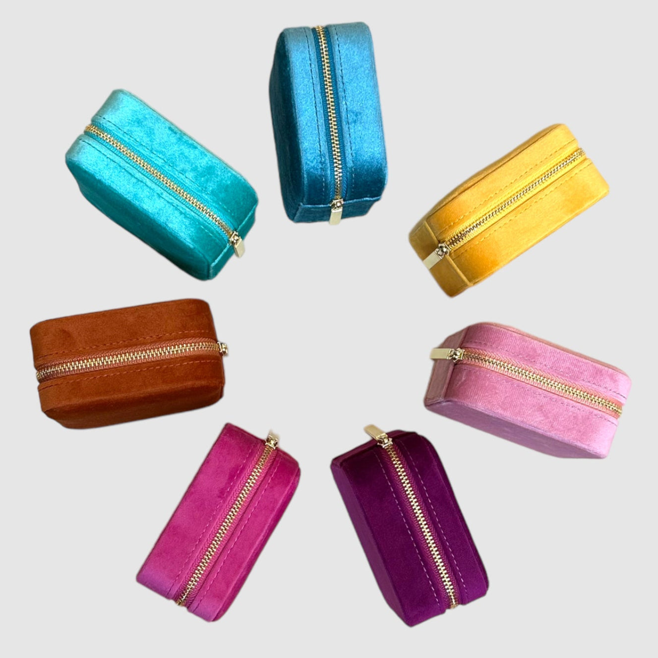 A collection of velvet jewelry cases with gold-colored zippers, displayed in various colors including blue, yellow, brown, pink, and purple.