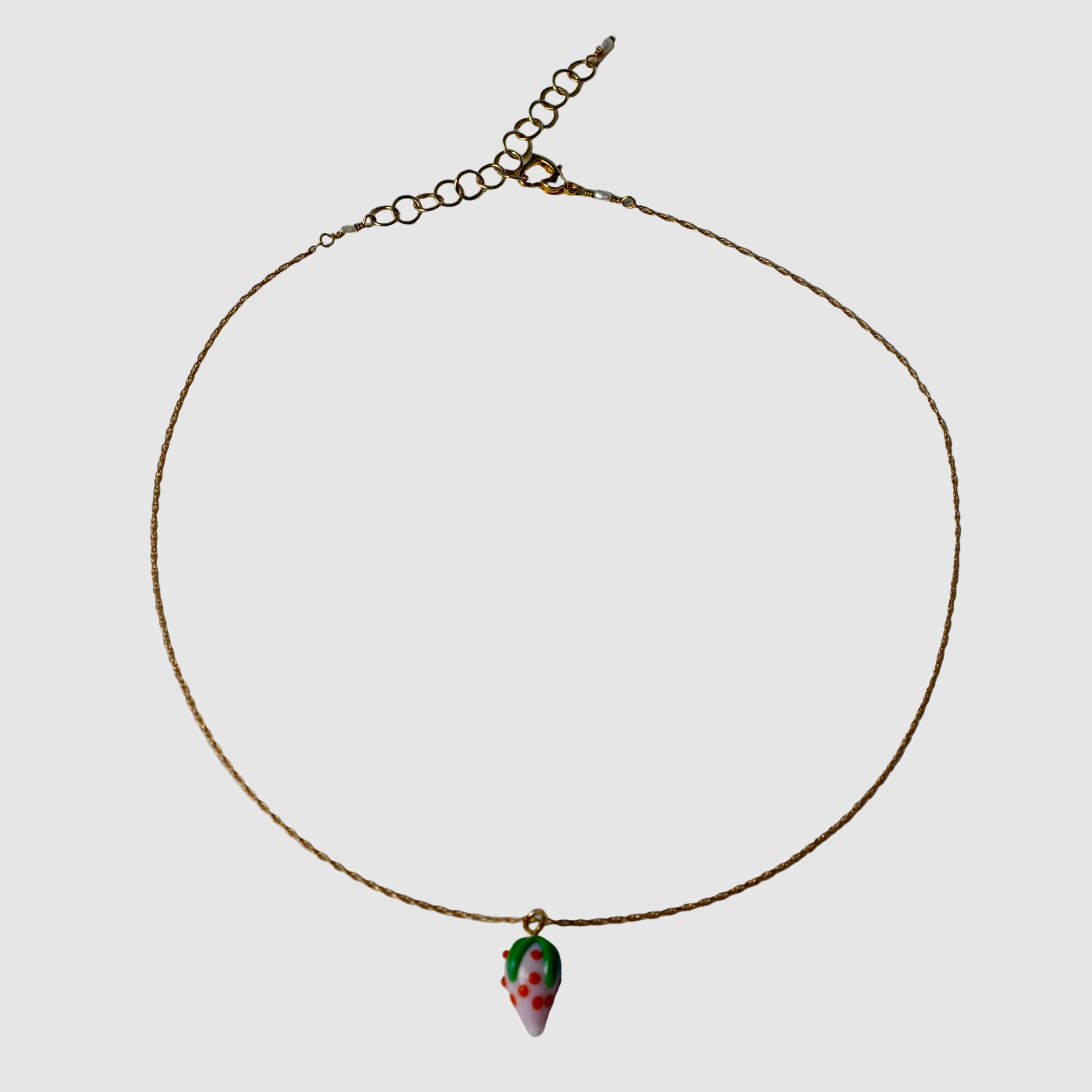 Gold necklace with a small glass strawberry pendant on a plain background