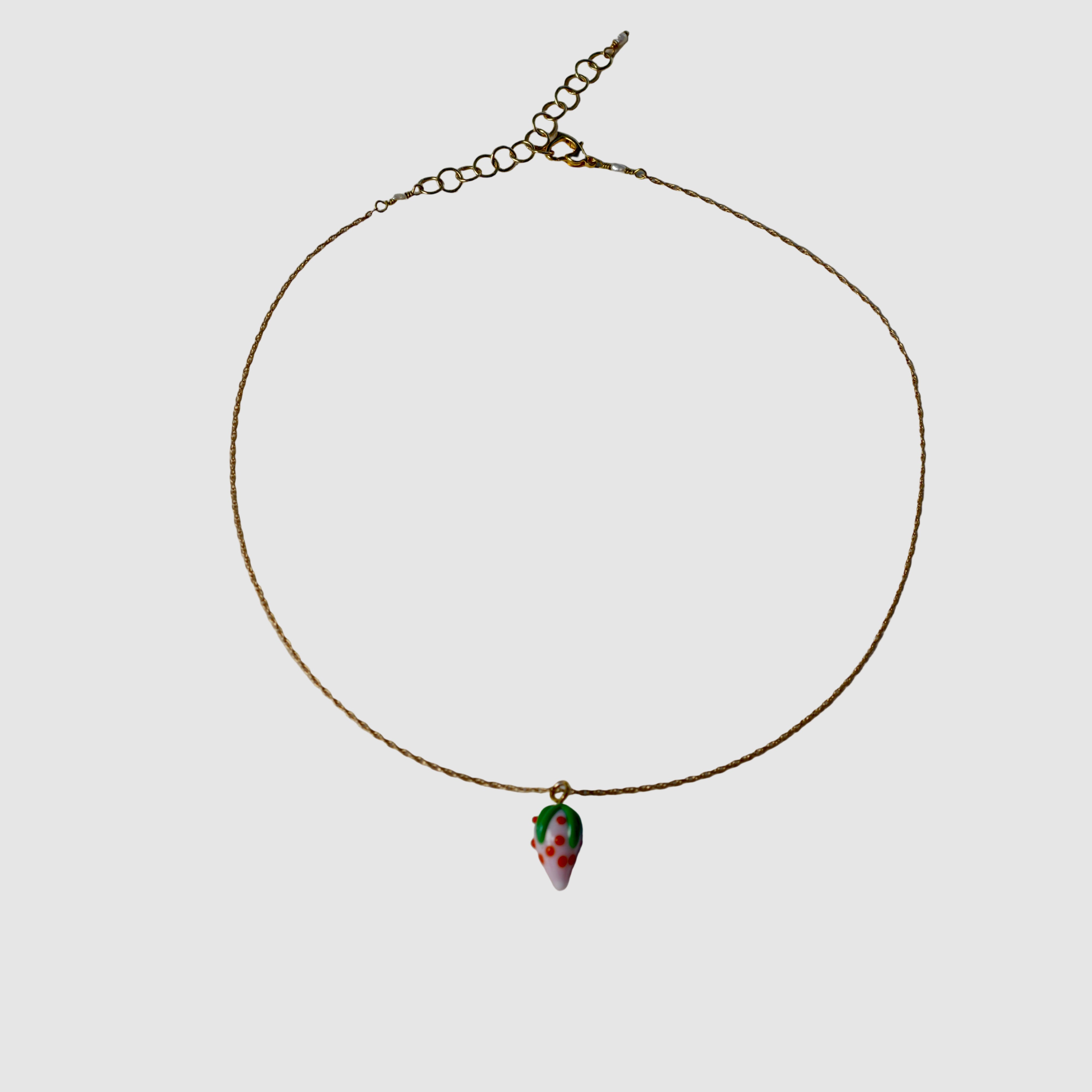 Gold necklace with a small glass strawberry pendant on a plain background