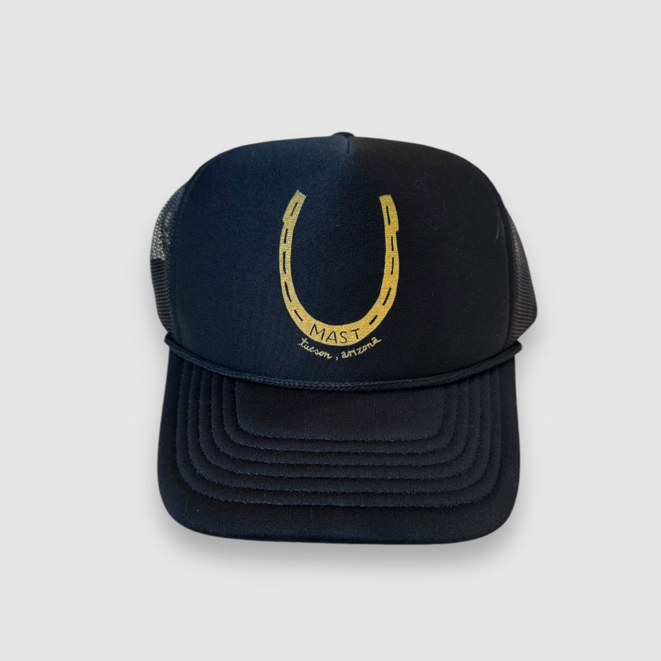 Black baseball cap/trucker hat with foam front and mesh back.  Hand drawn yellow horseshoe design, facing up with MAST in center and Tucson, Arizona  printed below. 