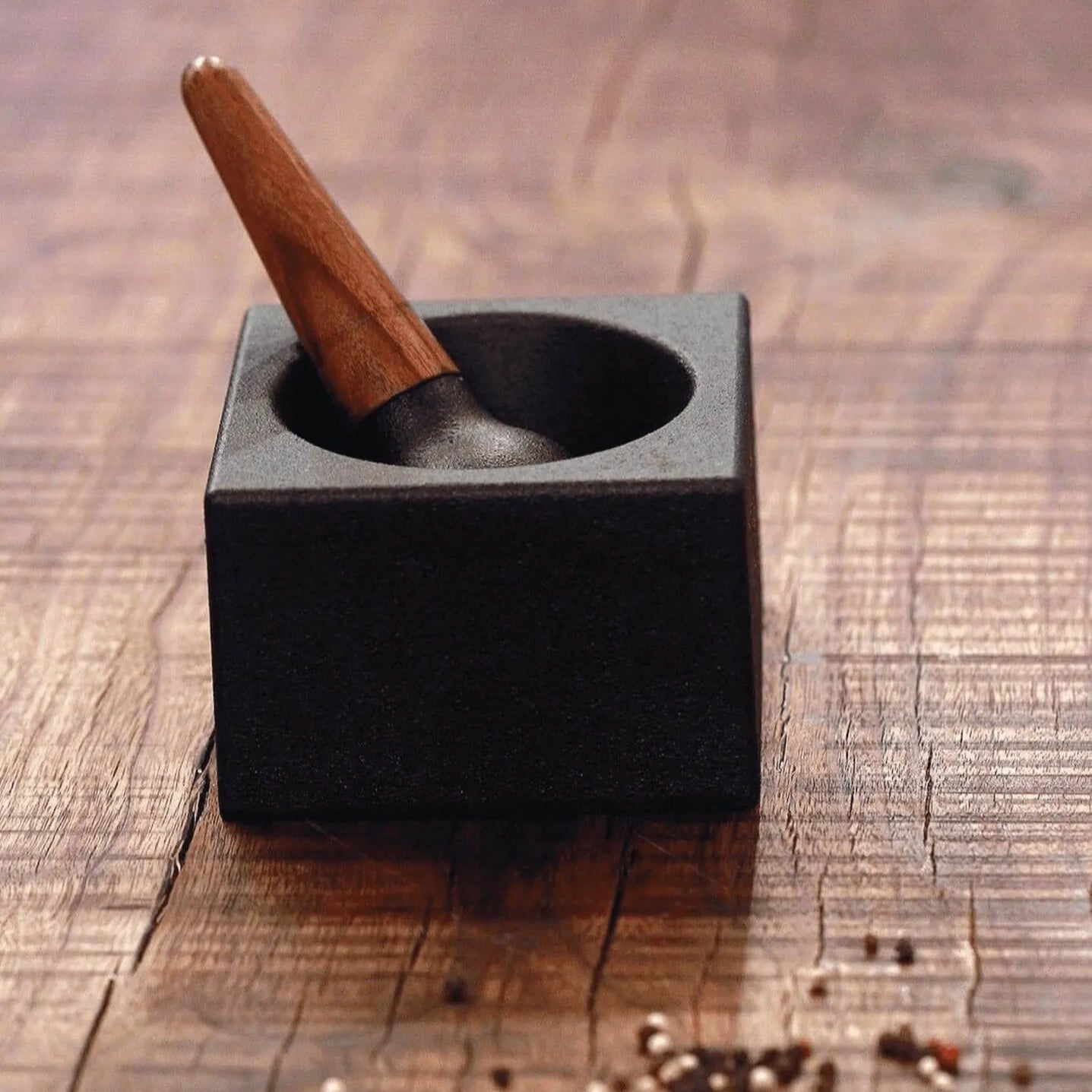 Mortar and pestle on a wooden surface with scattered spices