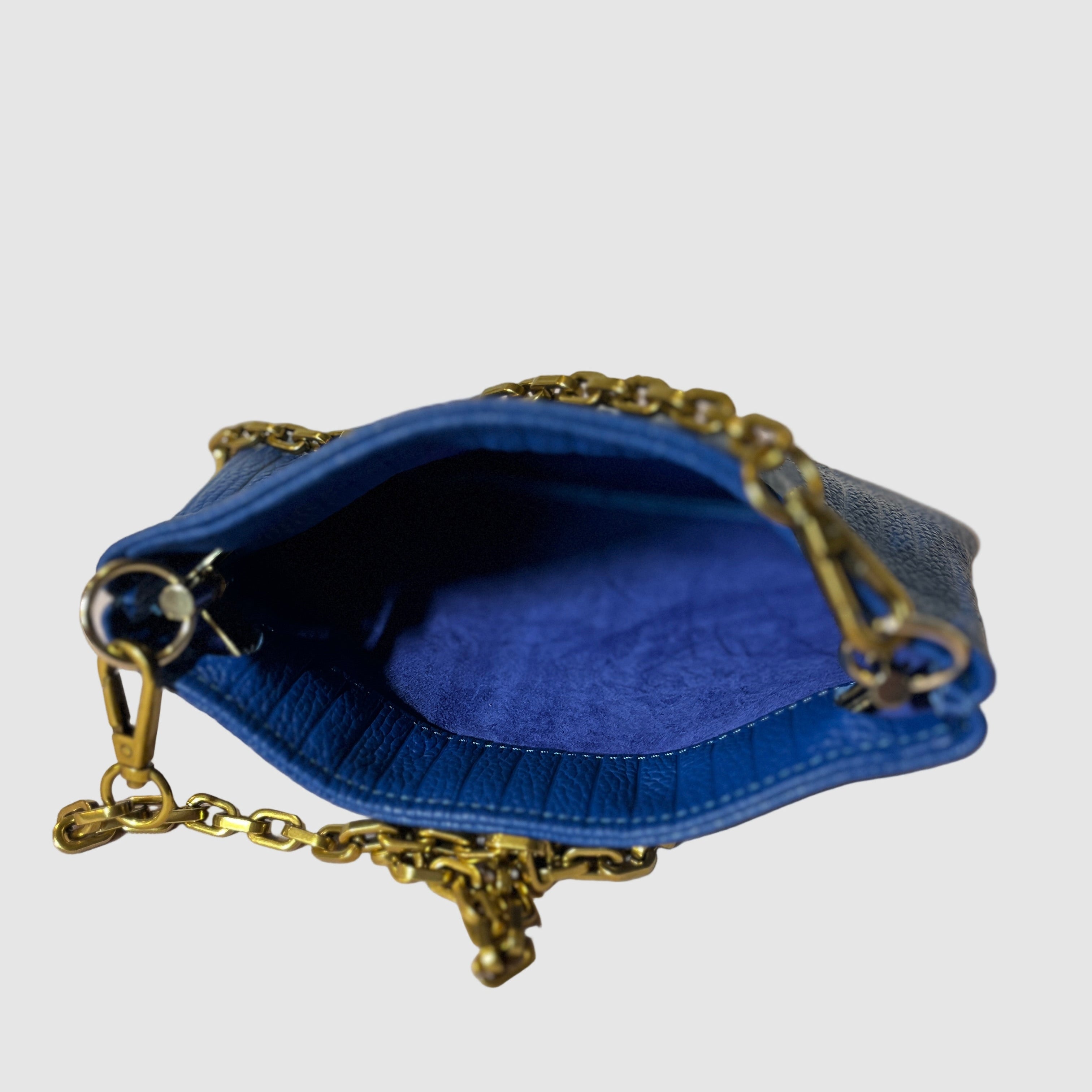 Suede blue interior shot of an embossed cobalt blue handmade leather handbag with curb chain strap on a light grey background. Bag made by Mellow Dawn in Tucson, Arizona. 