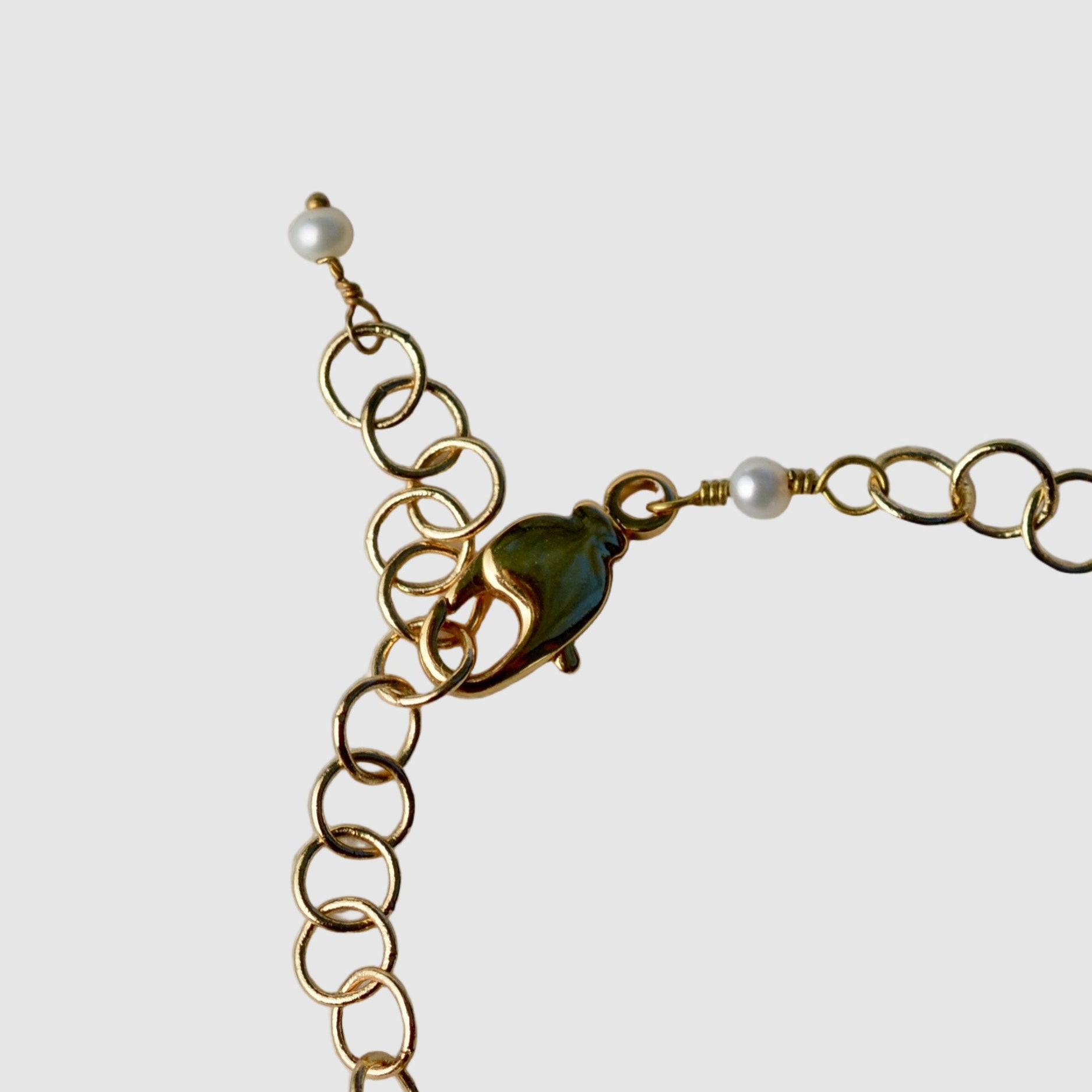 Gold chain bracelet with a green and silver charm on a light gray background