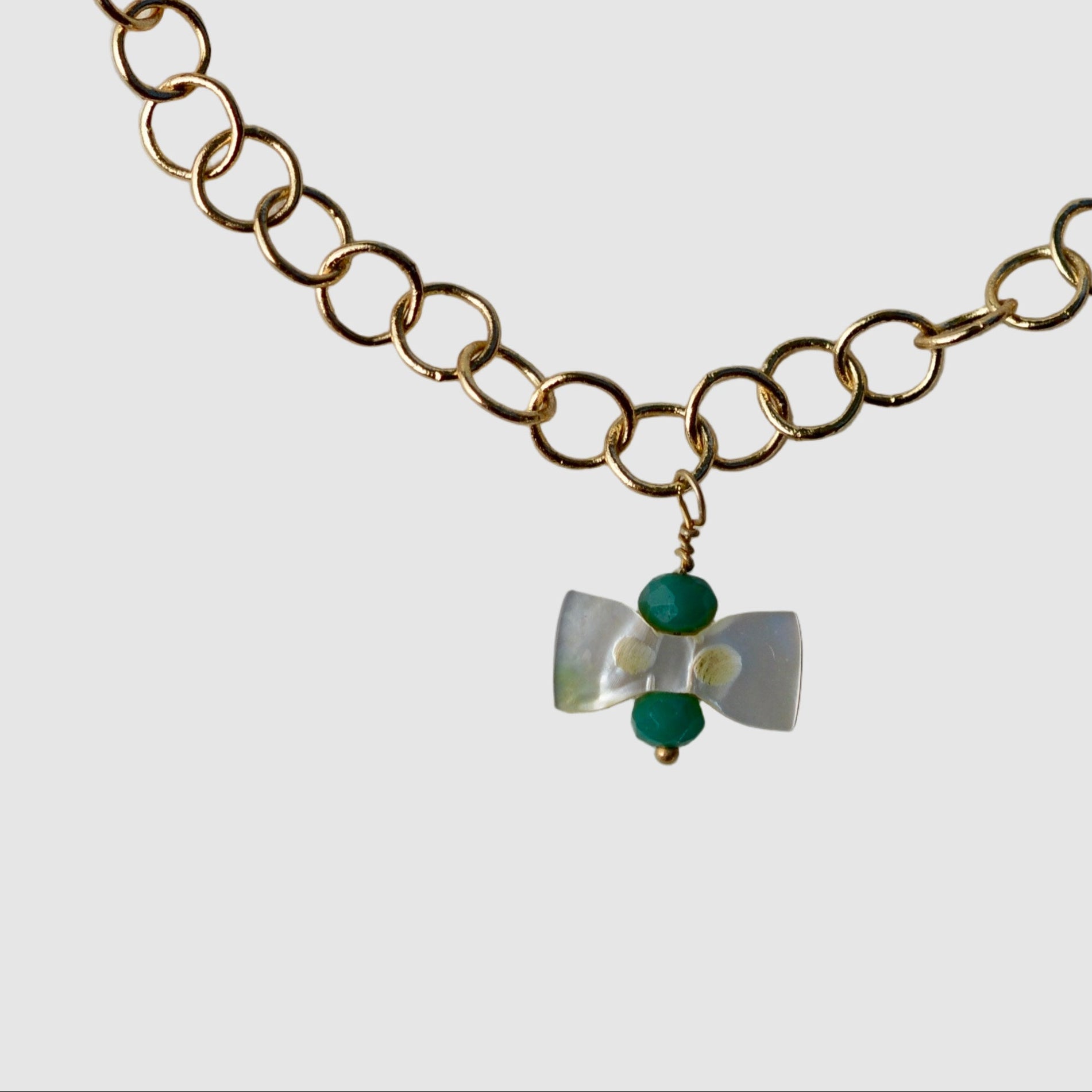 Gold chain bracelet with a green and silver charm on a light gray background