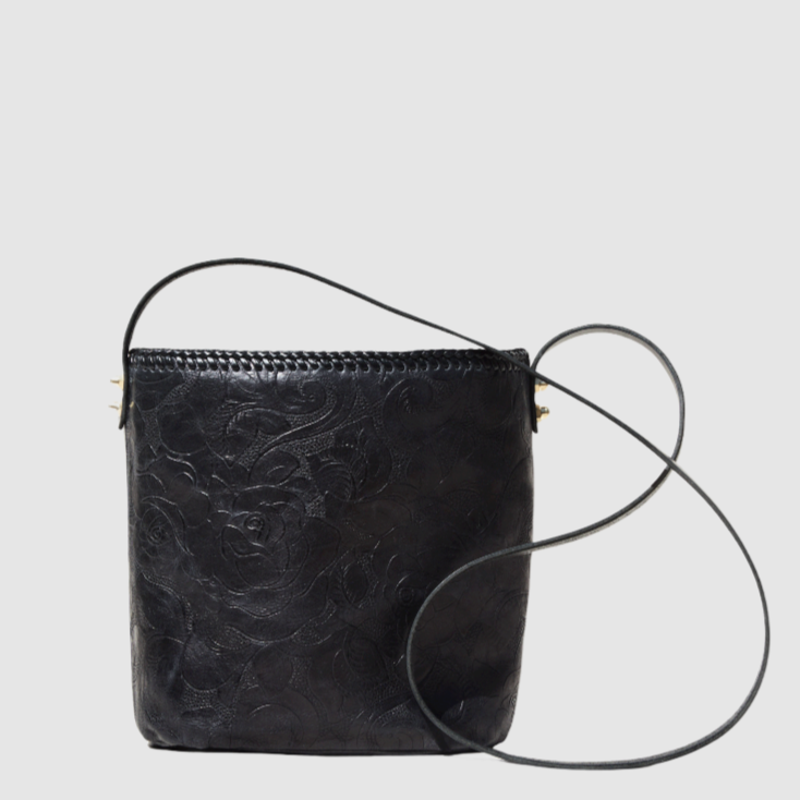 Black leather bucket bag with a single strap and top handle, featuring rose embossed design and brass acorn detail.