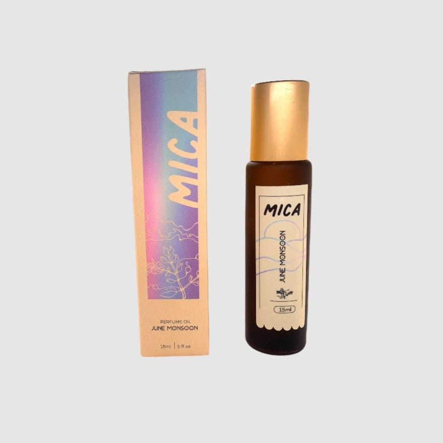A product image featuring a roller ball perfume applicator with a gold cap next to its packaging box. The packaging has a colorful design and the brand name 'MICA' is visible.