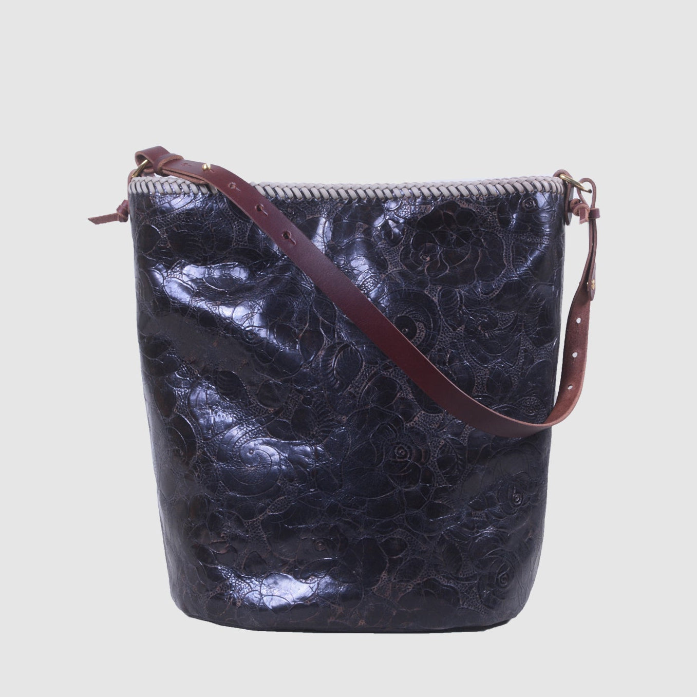 A medium-sized chocolate brown leather bucket bag with a rose embossed pattern, a burgundy leather strap, and visible stitching details handmade in Tucson by Mellow Dawn, one of the founders of MAST