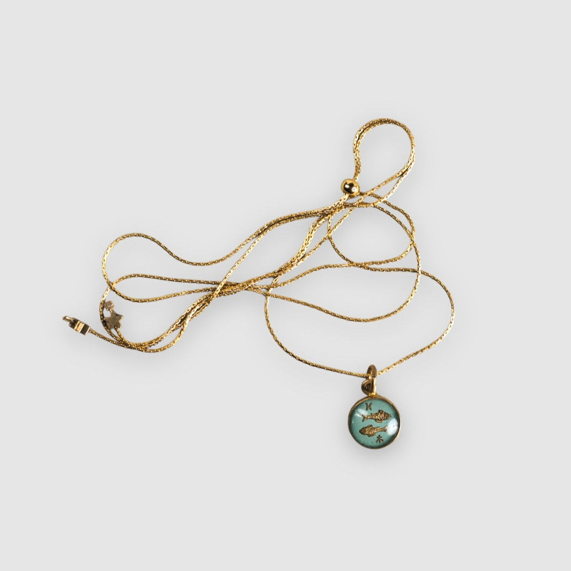 Gold necklace with a green pendant on a light gray background