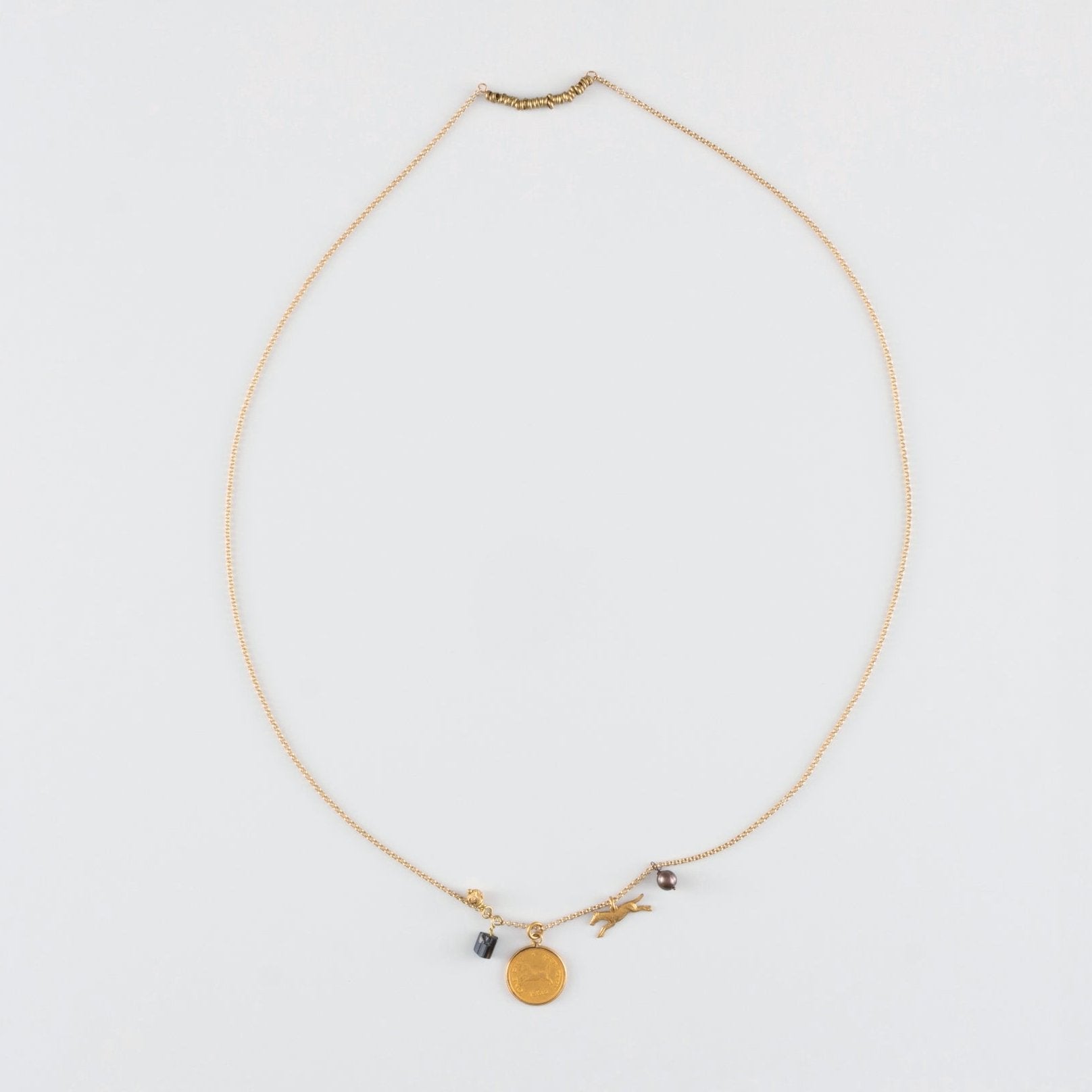 A necklace with a vintage bronze horse charm and accent charms, featuring faceted blue glass beads and a gold-colored chain.