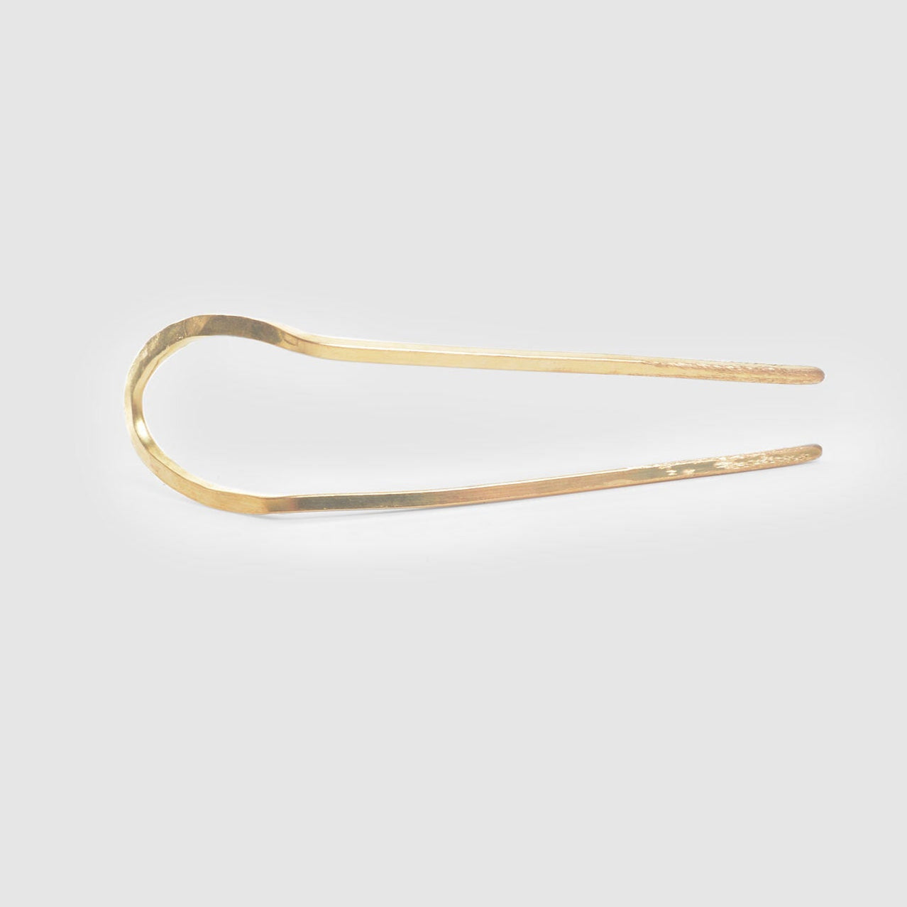 A regular length hand hammered brass hairpin from Tasha Bundy's ARCO collection on a light grey background.