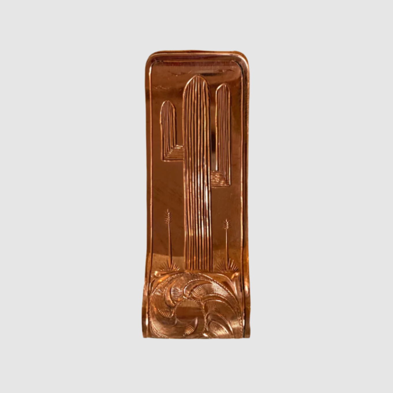 A hand engraved copper money clip with a saguaro design on it.