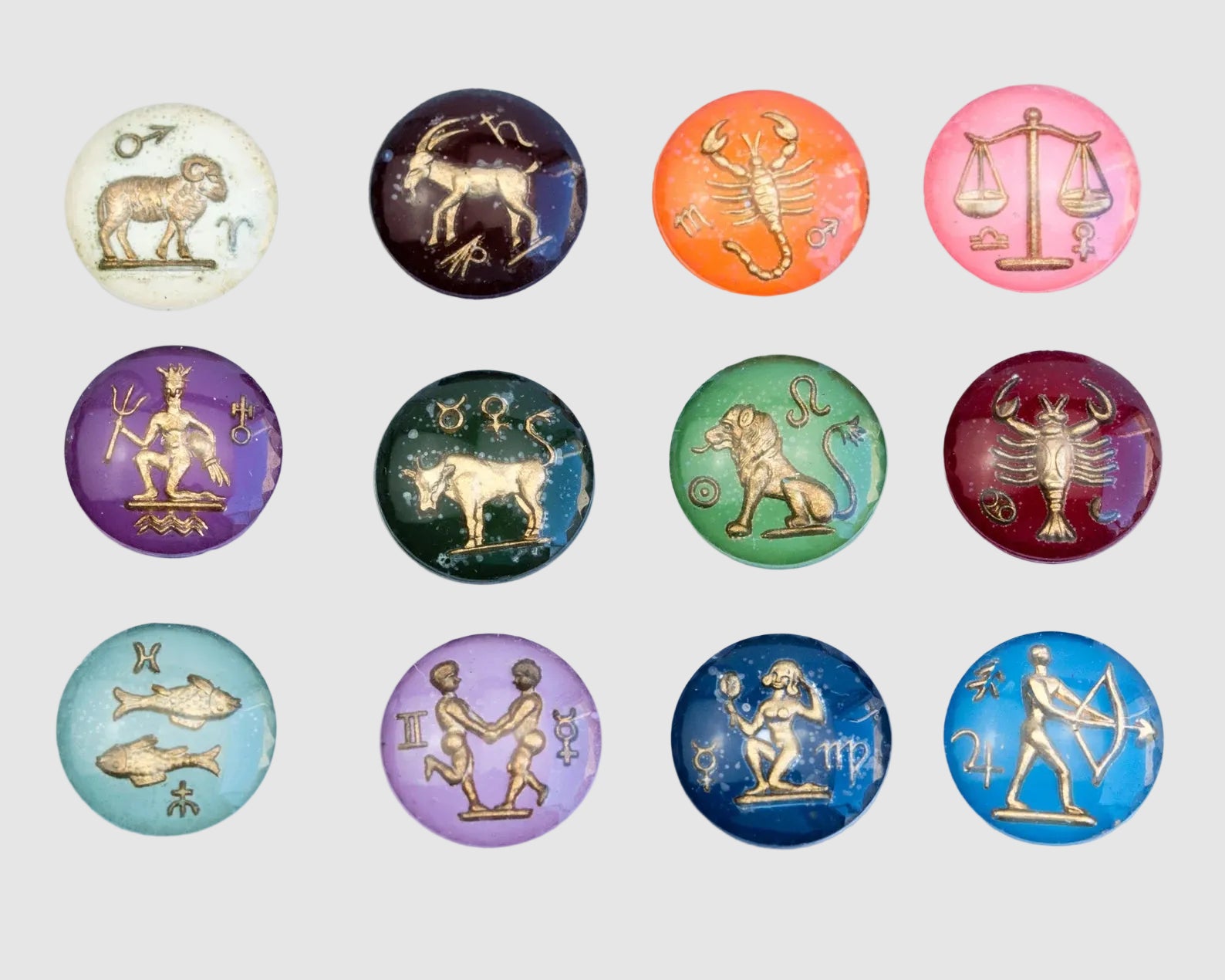 Set of glass zodiac pendants with each sign depicted in a circular design on a light grey background.